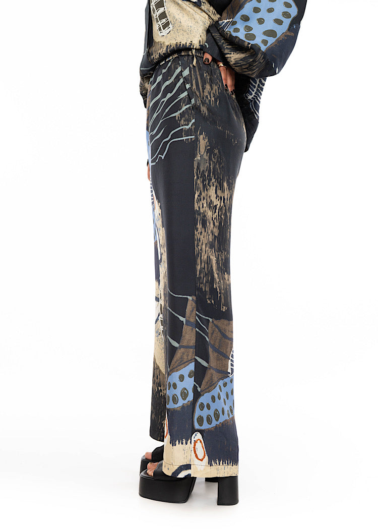 A close up of a model wearing a wide leg Silk trousers. Standing at a side angle; drawing attention to the trouser length.