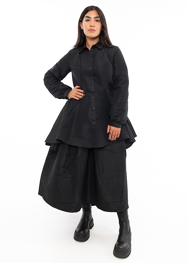 A Model wearing a Black structured Shirt with features including a collared neckline, buttons to fasten and balloon sleeves. Styled with a matching Black balloon Skirt and Black Boots.