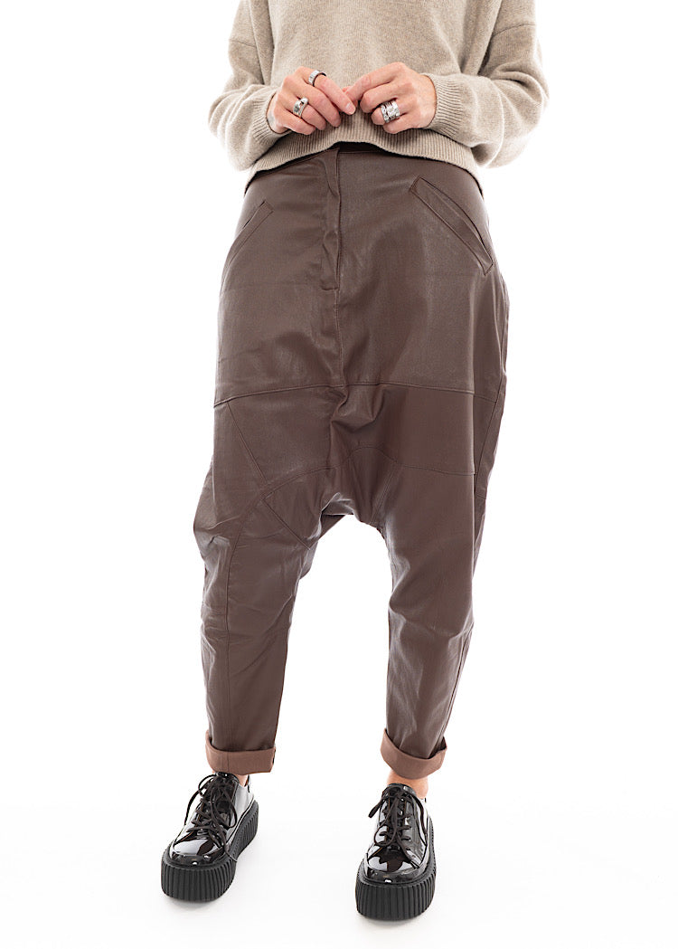 A Model wearing a Structured Drop-Crotch Brown Leather Trouser. Showing the curved seam-lines throughout the Trouser and fold up hem.