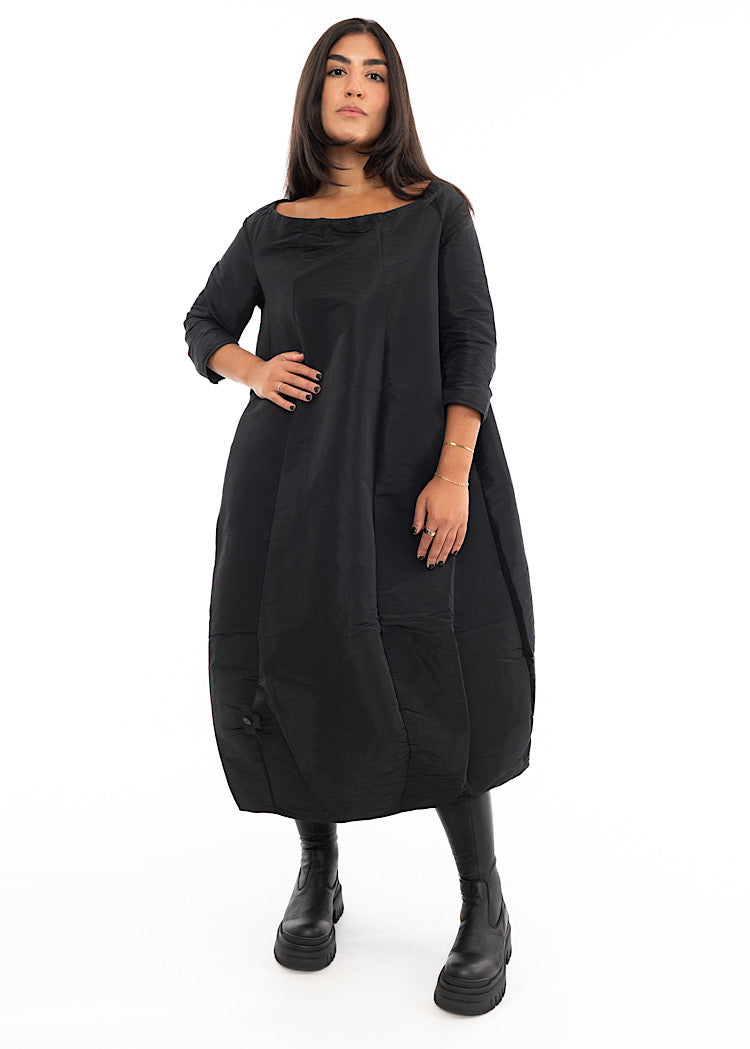 A Model wearing a Black structured balloon styled dress. Featuring a slash neckline, three-quarter length sleeves and side seam pockets.