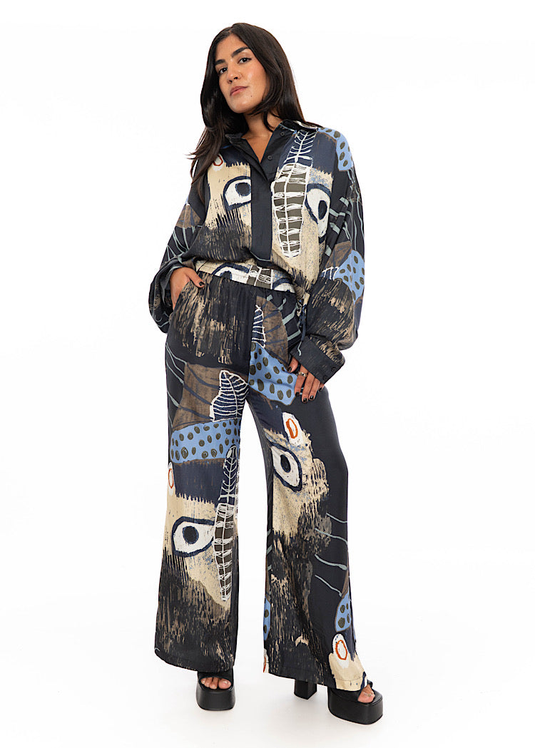 A model wearing a wide leg Silk trouser with a matching shirt. Standing facing the front disclosing the full outfit look. Paired overall with a black high heel.