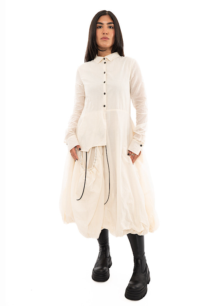 A full frame photo of A Model wearing a bubble skirted Dress in a creme colour. Focusing on the flap pocket, paired with a Black Boot.