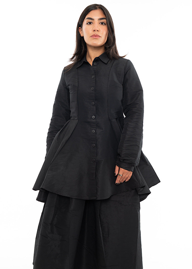 A Model wearing a Black structured Shirt with features including a collared neckline, buttons to fasten and balloon sleeves. Styled with a matching Black balloon Skirt.