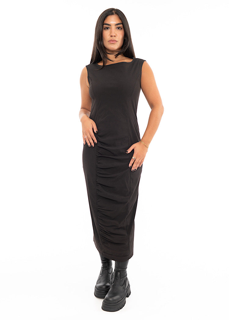 A Model wearing a fitted, sleeveless Dress in a washed dark Brown colour. Focusing on the ruching material along the bottom of the dress.