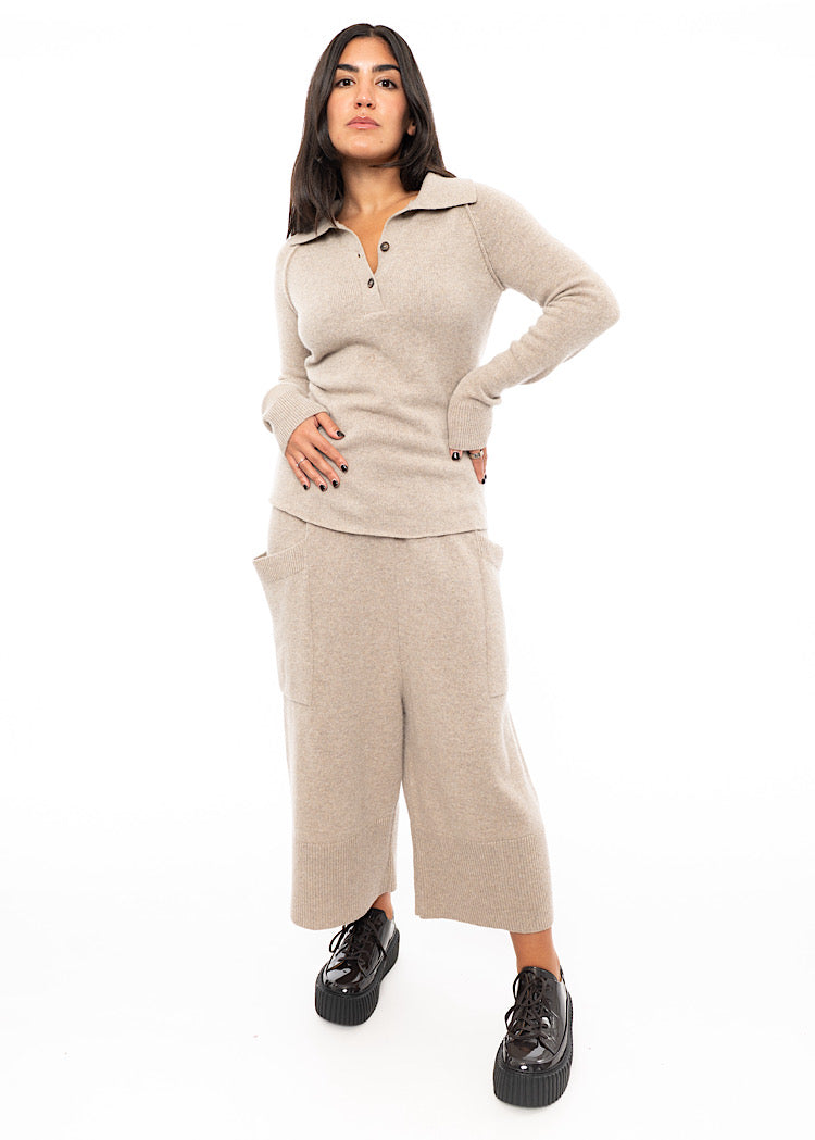 A Full Frame photo of A Model wearing a beige Pullover, featuring a V-neckline, buttons and a ribbed cuff. Paired with A Matching Trouser and patent shoe.