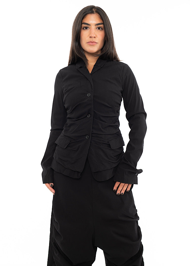 A Model wearing a minimalist techno Jacket and matching trousers, in a Black colour. Showing the fitted design.