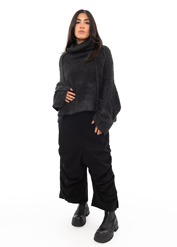 A full size photo of A Model wearing a washed Grey Pullover, including features of a turtle neck and wide long sleeves. Paired with Black Trousers and Boots.