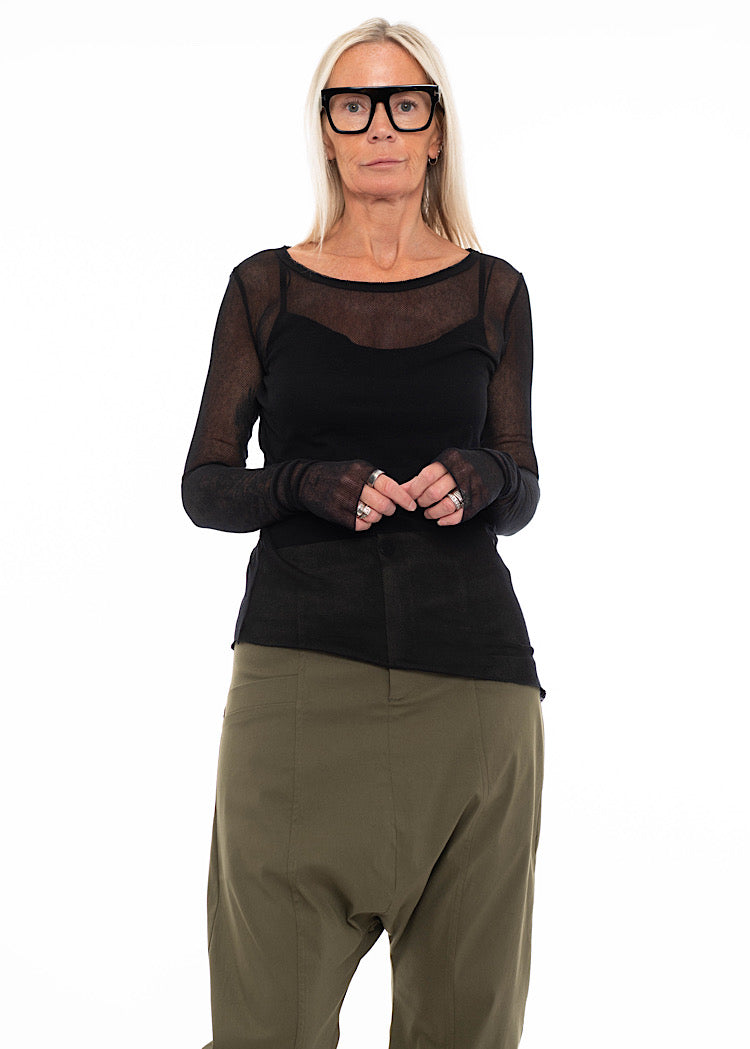 Model wearing black sheer mesh long-sleeve top with olive green drop-crotch cropped trousers and black combat boots.