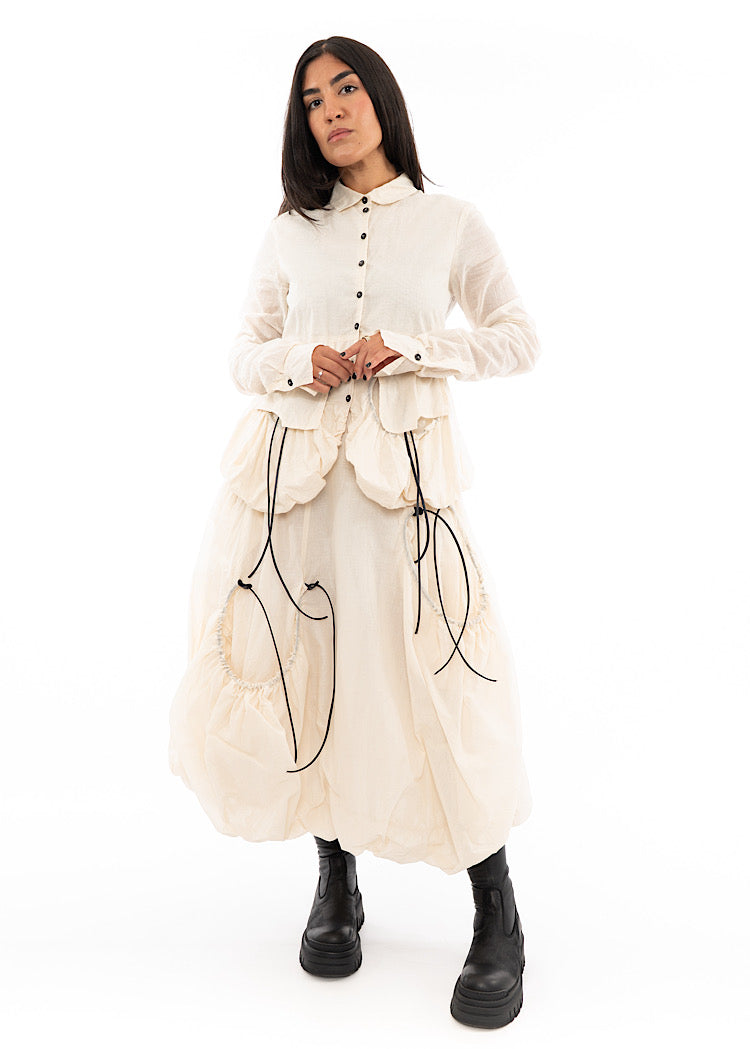 A full frame photo of a Model wearing a sculptural Jacket with a Skirt in the matching light beige colour. Focusing on the full outfit.