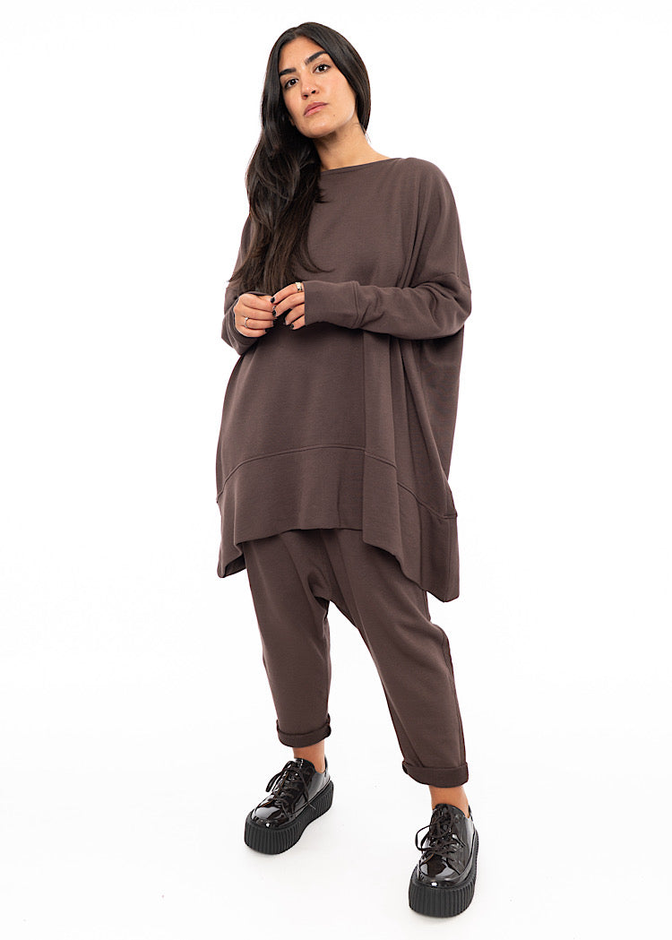 A Full frame Photo of A Model wearing an oversized Plum toned Pullover, with a long seam-line throughout the piece.