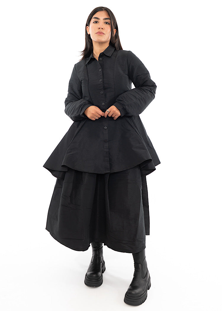 A full frame photo of A Model wearing a Black Structured Skirt, paired with a matching Blouse and Black Chunky Boots. Focusing on the volume of the outfit.