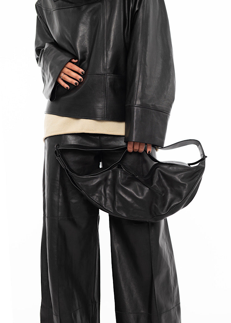 Close up of Model wearing a black Leather jacket, with black Leather straight leg trouser and beige pullover. Focusing on Black Slouchy leather bag with a long strap and a shorter strap.