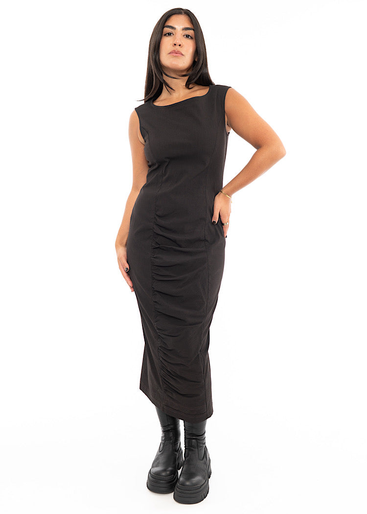 A Model wearing a fitted, sleeveless Dress in a washed dark Brown colour. Focusing on the ruching material along the bottom of the dress.