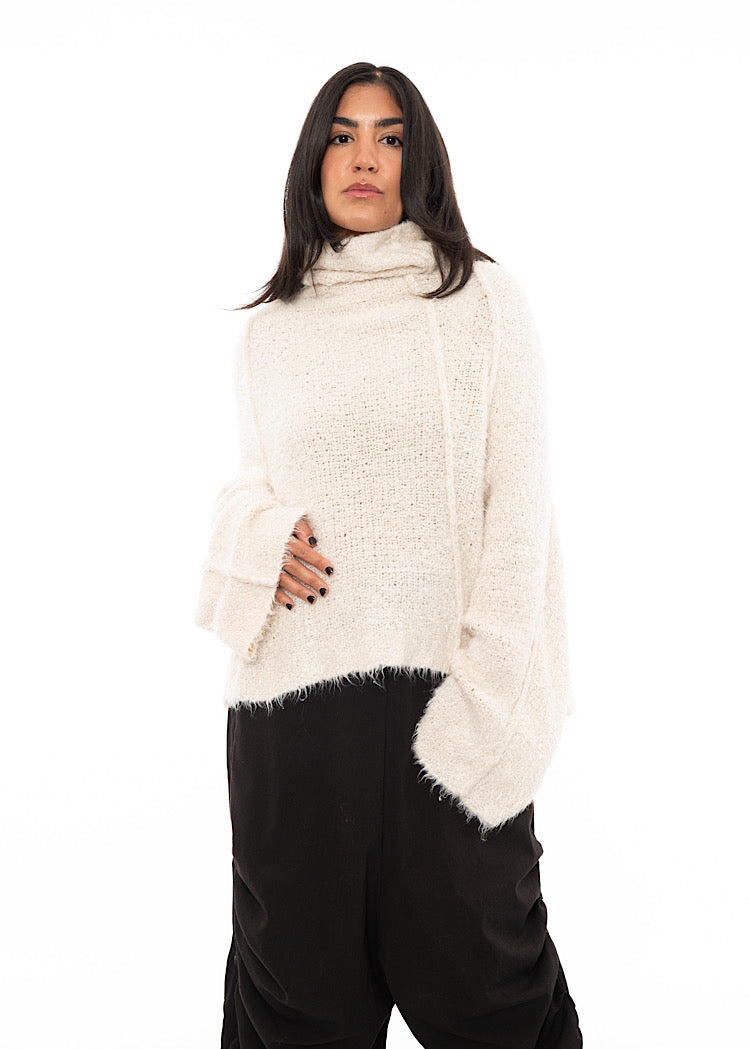 A Model wearing a Light creme Fluffy pullover featuring a turtle neck feature and an oversized fit. Paired with Black trousers.