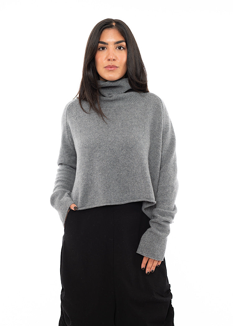 A Model wearing a Grey Pullover, featuring a turtle neck and a straight fitted jumper. Paired with a Black Trouser.