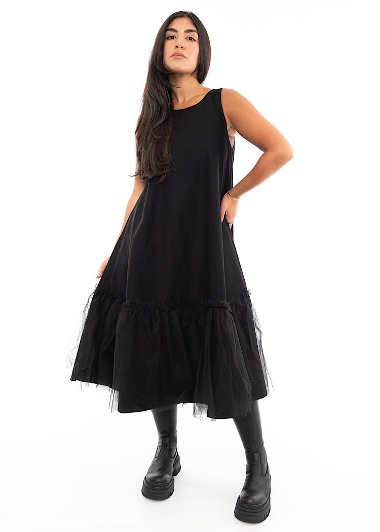 A Model wearing a fitted Black dress which bottom hem turns into a floaty mesh skirt. Styled With Black Boot.