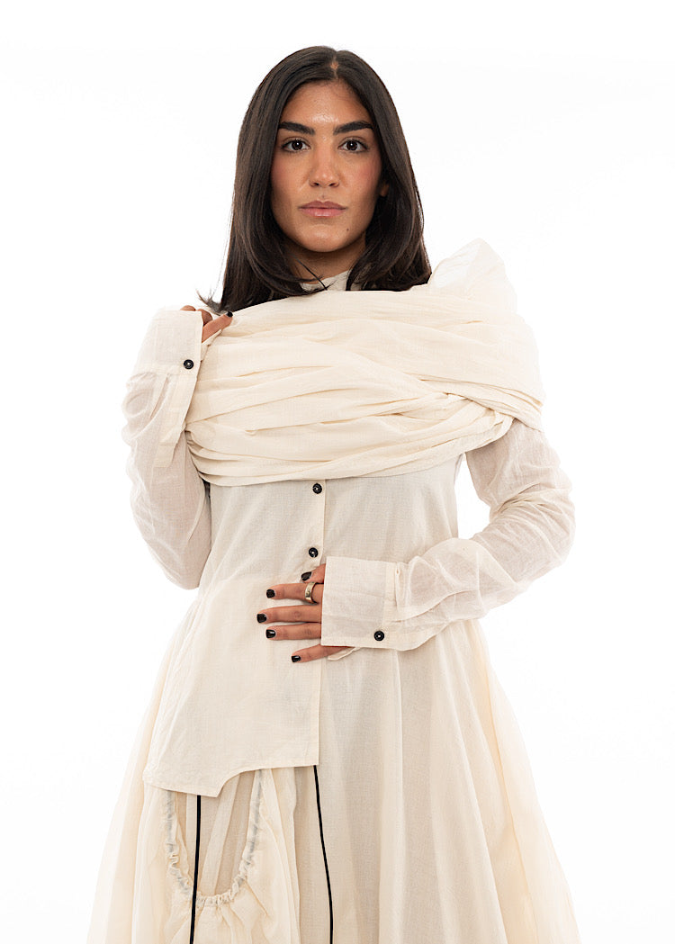 A Model wearing an oversized Scarf over her shoulders adding volume to the matching Dress in a light beige colour.