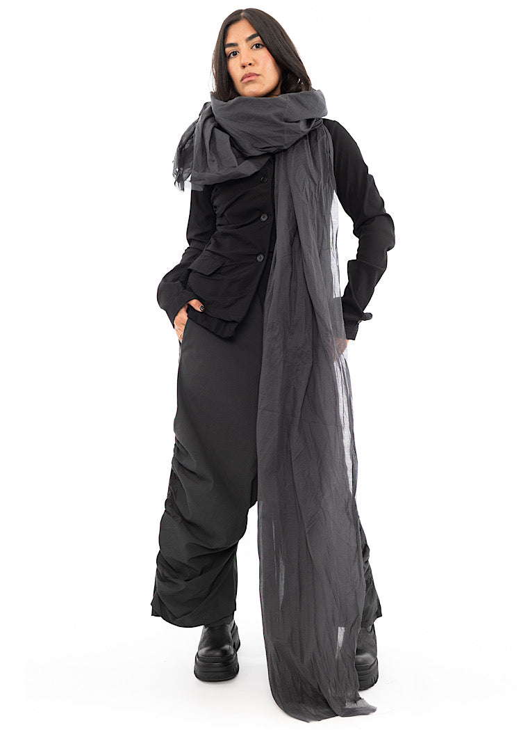 A full frame photo of A Model wearing an oversized long Washed Grey Scarf, styled over her with a Black Jacket and Black Boots.