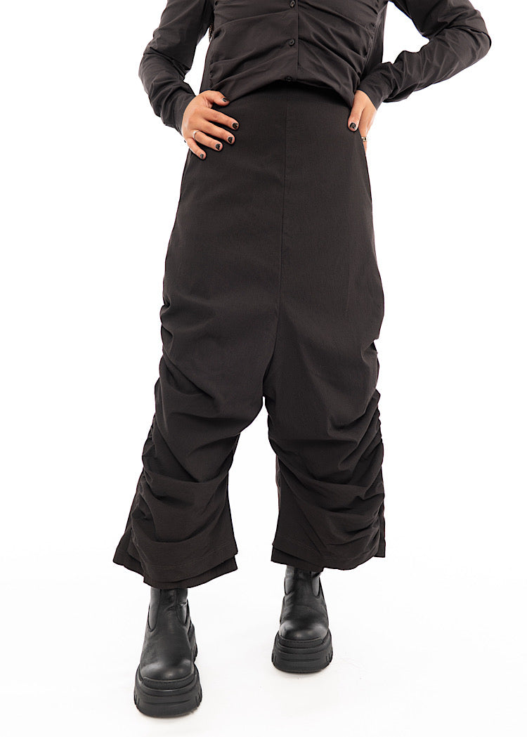 A Model wearing a drop-crotch Trouser in a washed dark Brown colour. Showing the distinct rouging effects on the Trouser leg.