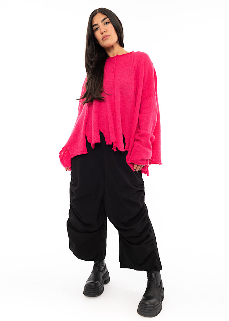 A full size photo of A Model wearing a Bright Pink oversized Pullover. Shown with a Black fitted trouser and Black Chunky Boots.
