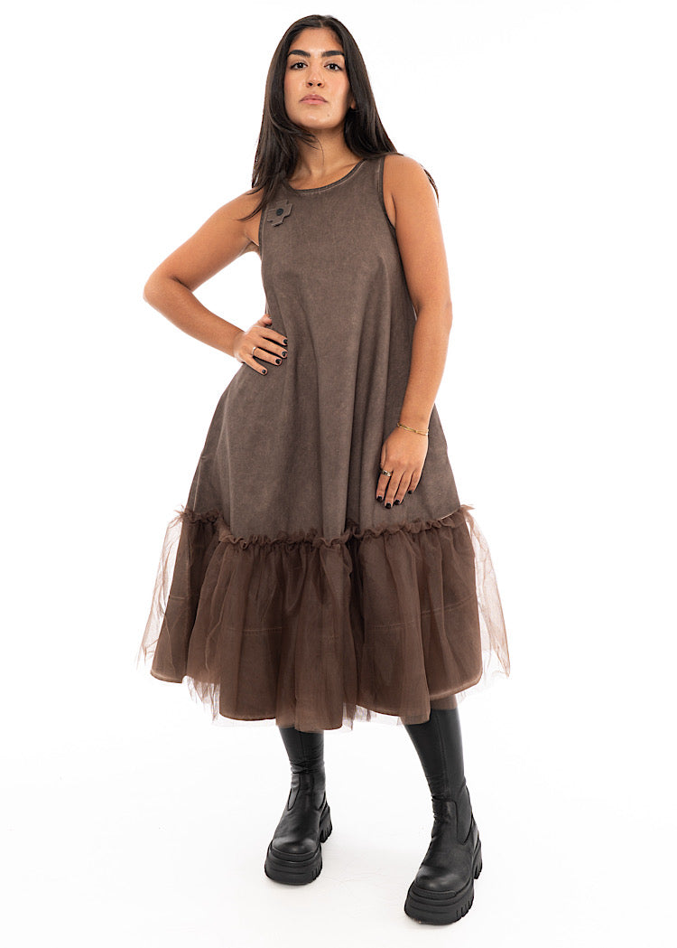 A Model wearing a Chocolate Brown sleeveless A-line dress with a matching Brown mesh layer close to the hem of the dress.Styled with a chunky black boot.