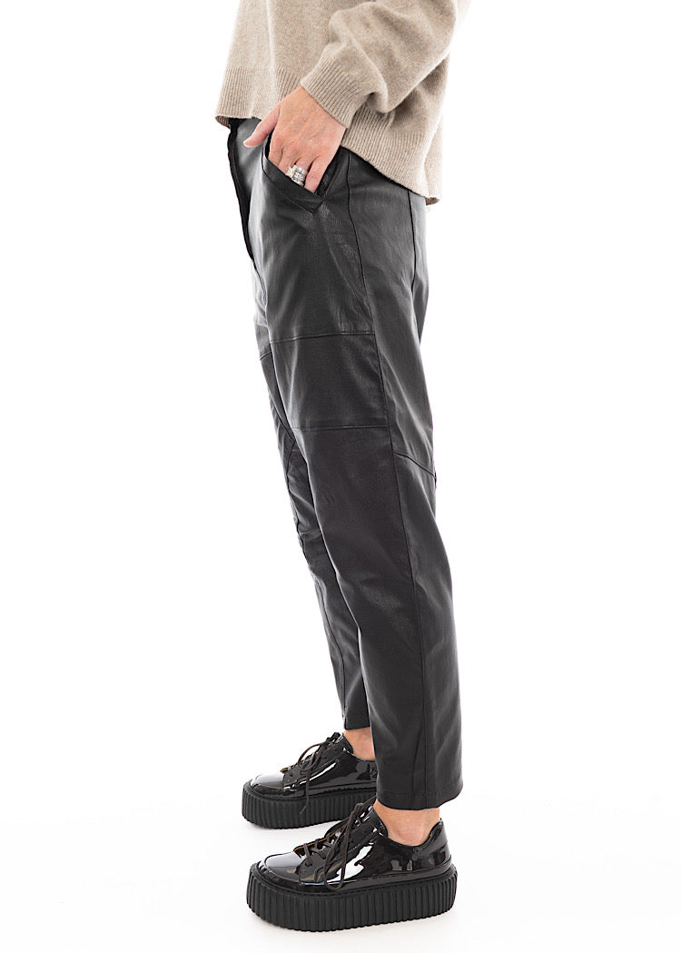A Model standing to a side wearing a Structured Drop-Crotch Black Leather Trouser, disclosing the pockets. Showing the straight seam-line.