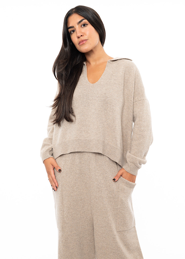 A Model wearing a light Beige knitted pullover with a ribbed hem, a deep V-neckline and a relaxed collar. Styled with a matching Trouser.