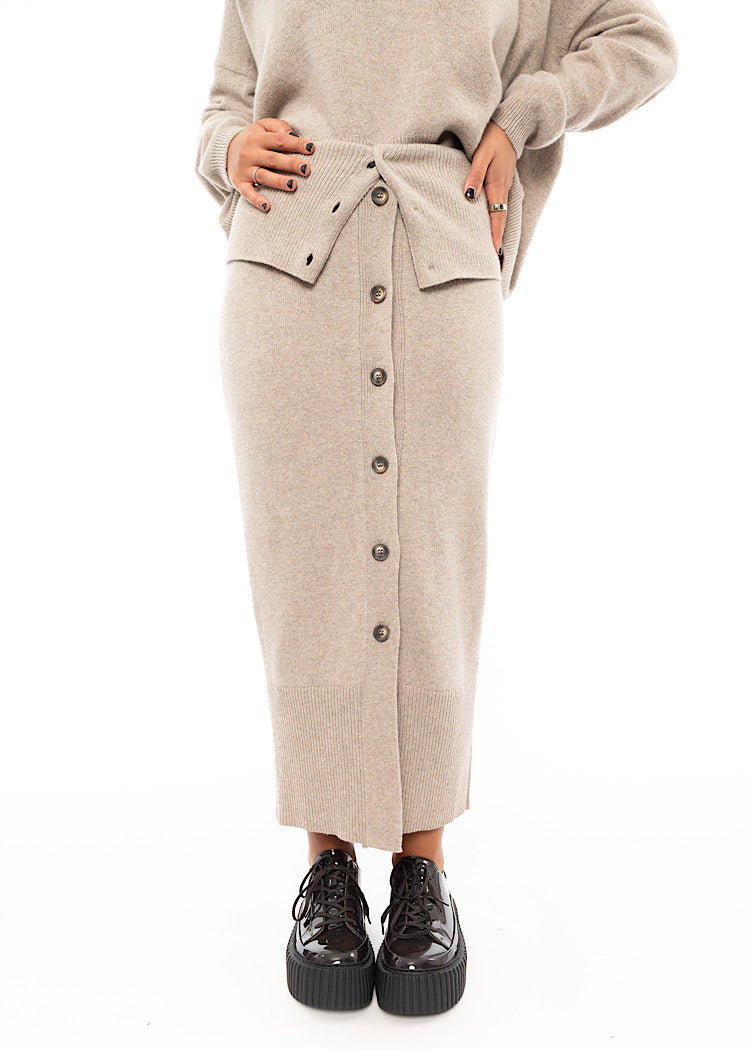A Model wearing a light beige completely buttoned up Skirt. Showing the Skirt in full.