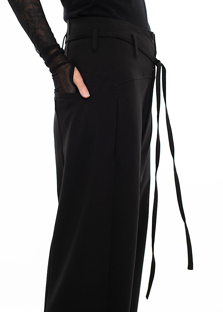 Close up of  wearing black drop-crotch trousers with side and rear pockets, with belt loops and drawstring detail, styled with mesh-sleeve top and combat boots.