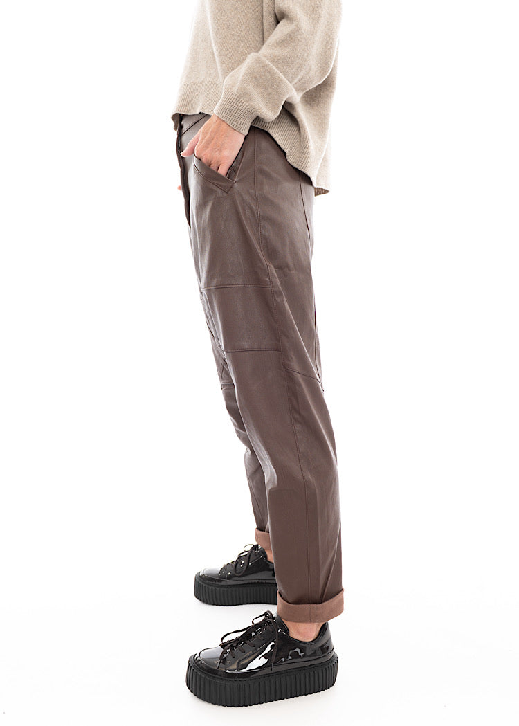 A Model standing to a side wearing a Structured Drop-Crotch Brown Leather Trouser. Showing the width of the trouser.