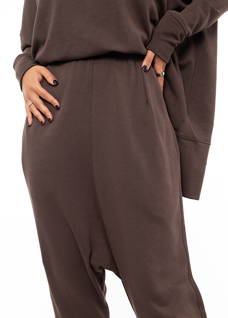 An up close of A Model wearing a plum toned drop-crotch trouser with a slight rolled up effect on the Ankle. 
