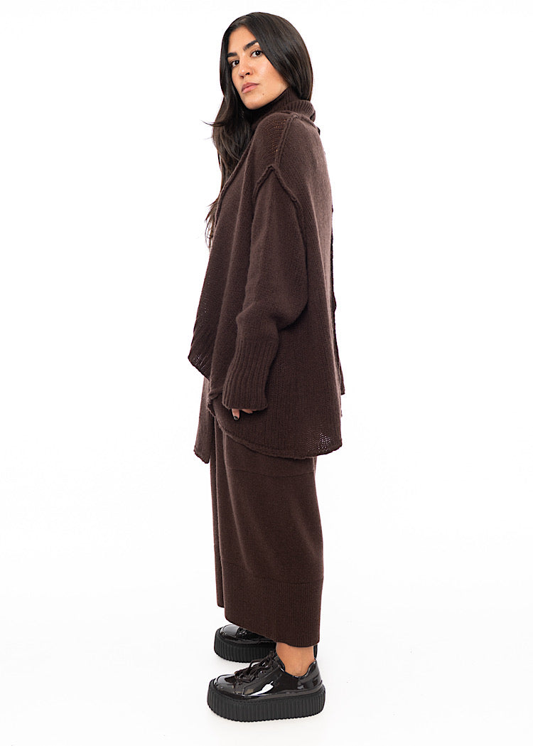 A Full frame photo of A Model standing to a side wearing a Brown Oversized pullover. Showing the arms length.