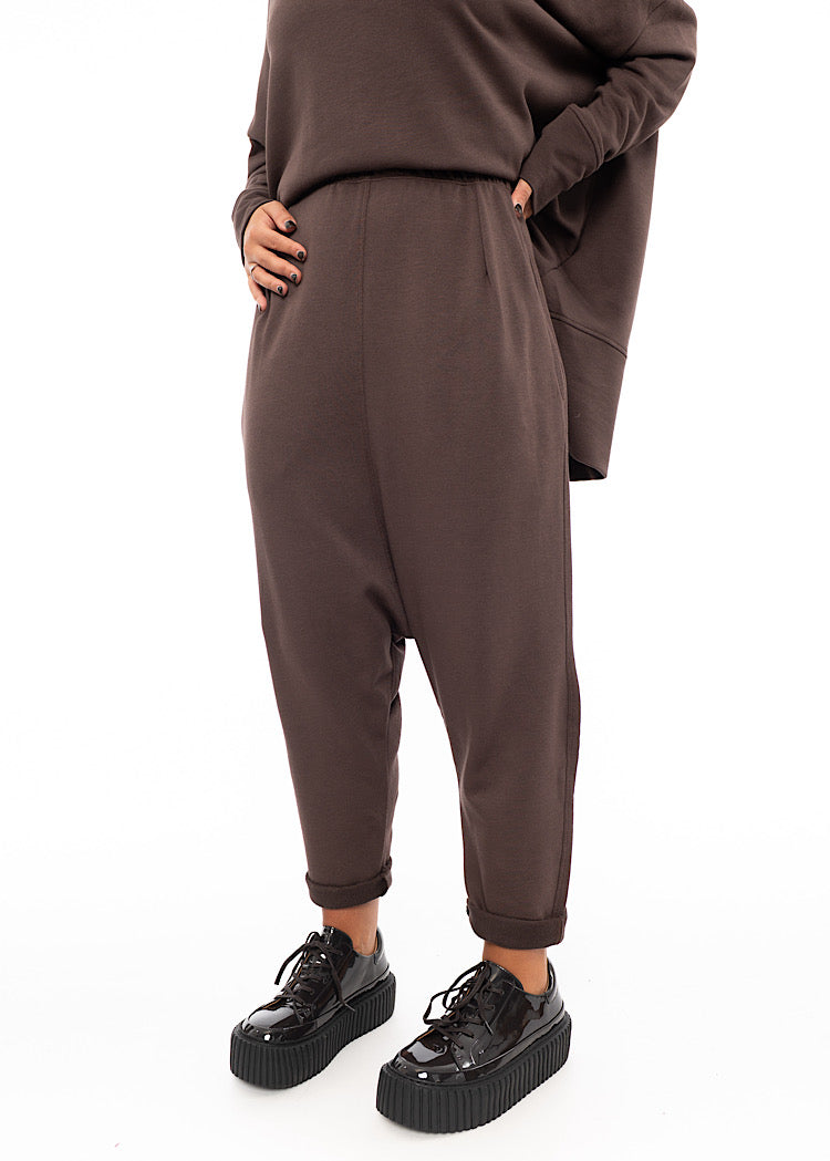 A Model wearing a plum toned drop-crotch trouser with a slight rolled up effect on the Ankle. Showing the straight fit of the trouser.