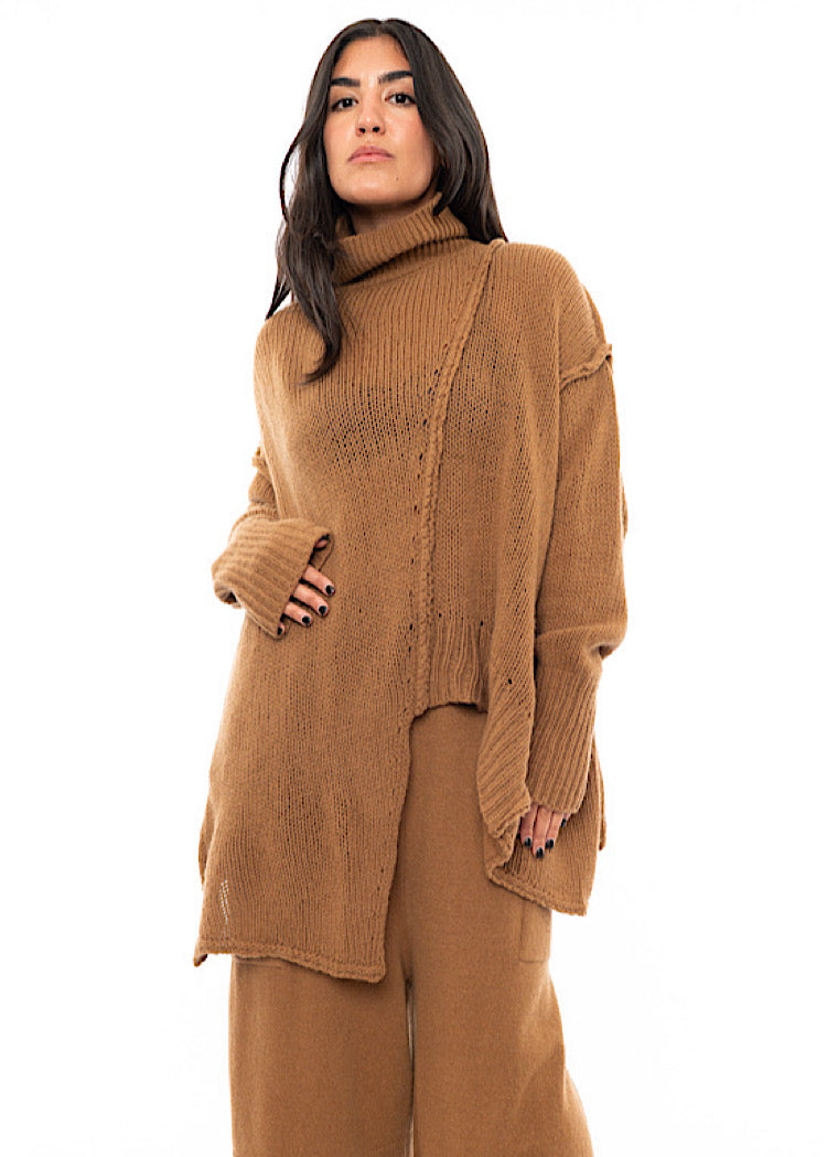 A Model wearing a light brown knitted Oversized Pullover with distressed pieces dangling down. Showing the ribbed cuffs.