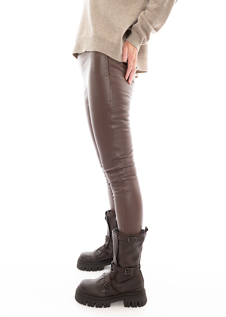 A Model standing to the side wearing a tight fitting Legging-Like Brown Leather Trouser. Showing the straight fit to them.