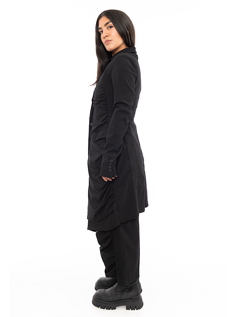 A Model standing to the side wearing a detailed techno coat and matching trousers, in a Black colour. Showing the fitted look from a different angle.
