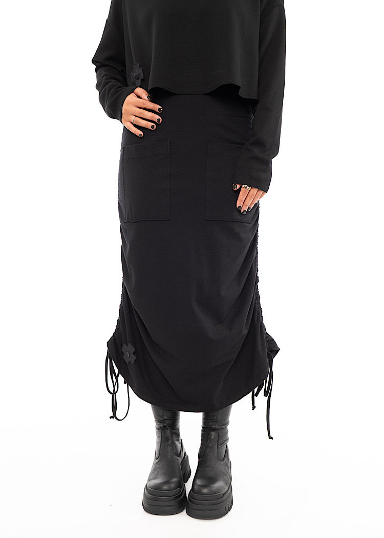 A Model wearing a Black drawstring Skirt, styled with a cropped Black Pullover and Chunky Black Boot.