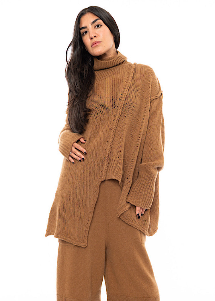 A Model wearing a light brown knitted Oversized Pullover with distressed pieces dangling down. Showing the distinct seam-lines in more detail.