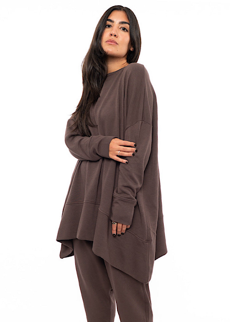 A Model wearing an oversized Plum toned Pullover, paired with a Matching Trouser. Showing the pieces long length of arm and body.