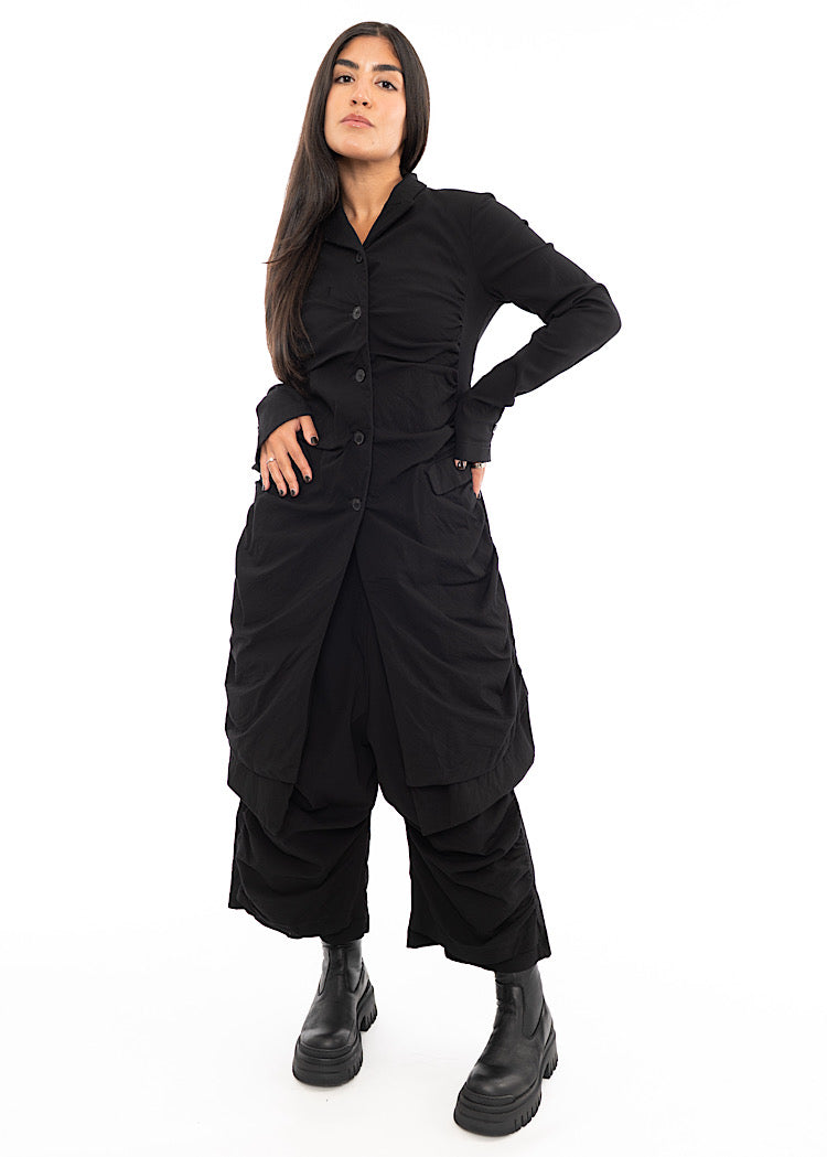 A full frame photo of A Model wearing a detailed techno coat and matching trousers, in a Black colour. Paired with a chunky soled black Boot.