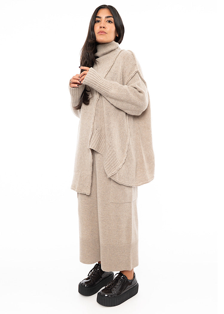 A full frame photo of A Model wearing a creme Knitted Pullover with  Distressed pieces throughout. Showing the oversized effect of the jumper.