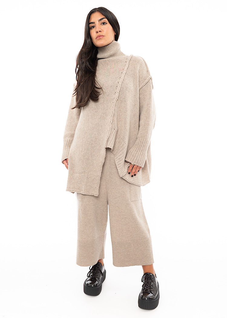 A full frame photo of A Model wearing a creme Knitted Pullover with  Distressed pieces throughout. Paired with a matching Trouser and patent Shoe.