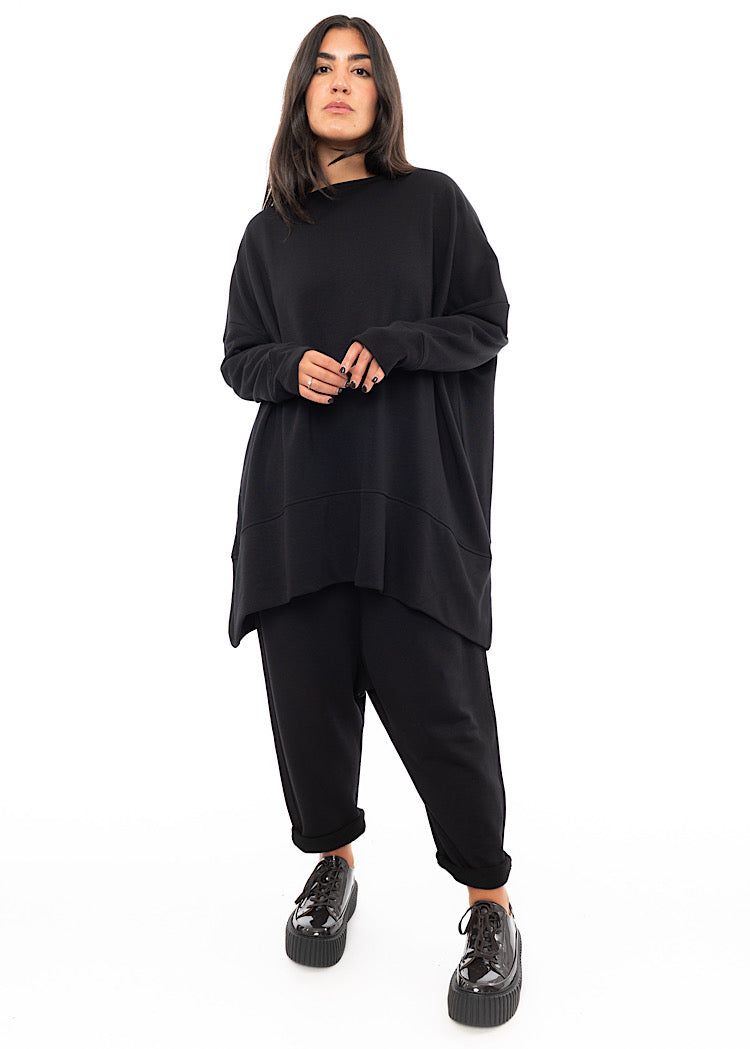 A Full frame photo of A Model wearing a slinky Black Oversized Pullover. Paired with a matching Trouser and Brown Patent shoe.