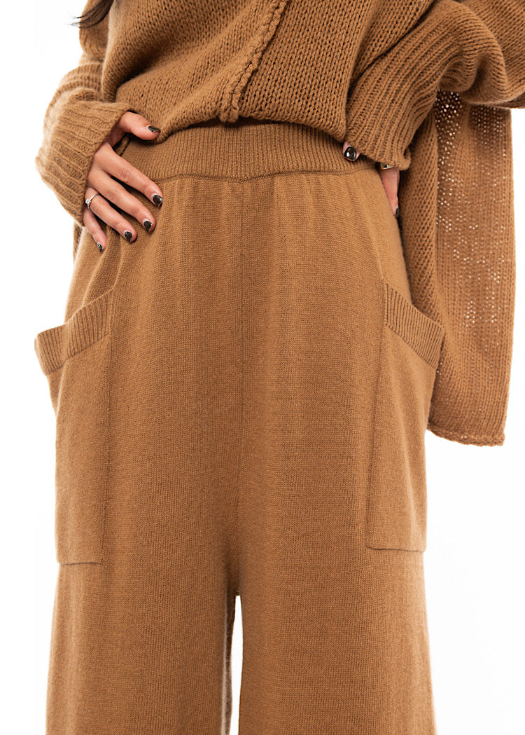 An up close of A Model wearing a Knitted pair of off-orange Trousers. Showing the waistband of the trouser.