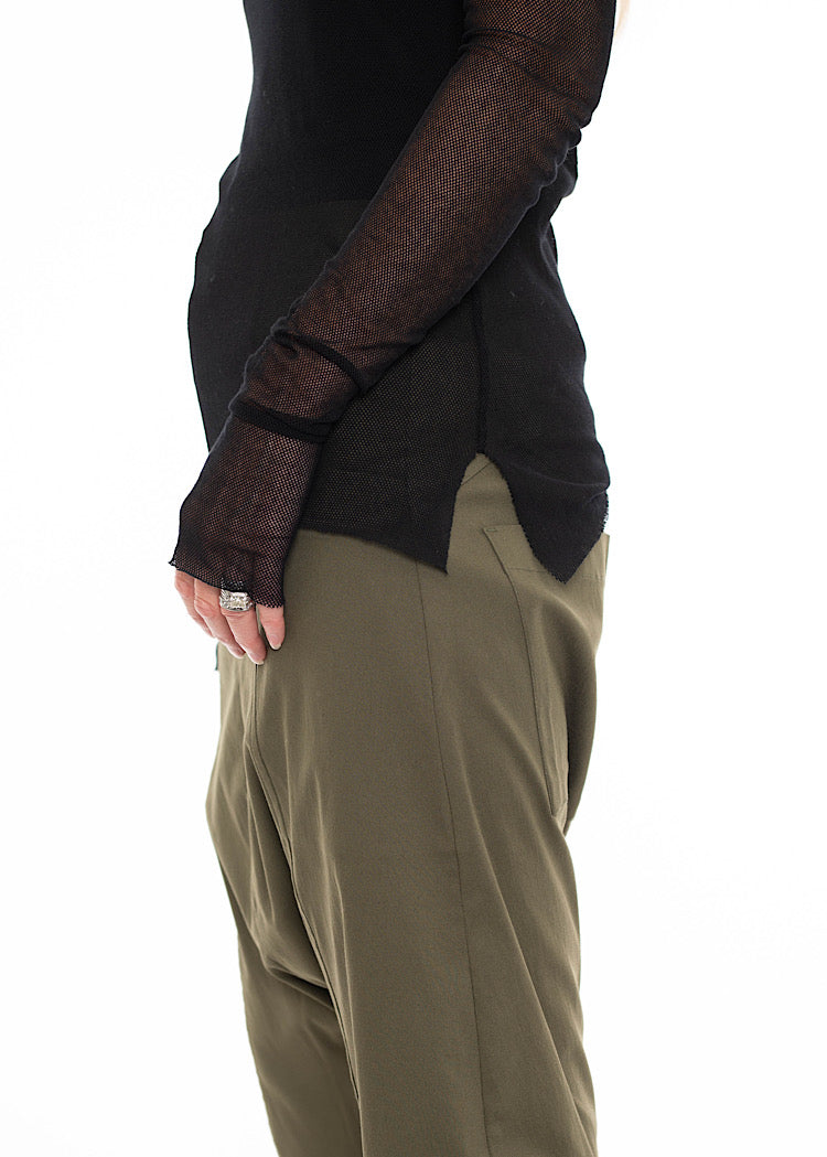 Close up of model wearing black sheer mesh long-sleeve top with thumb holes and side vents. Styled with Olive Green drop crotch trouser.