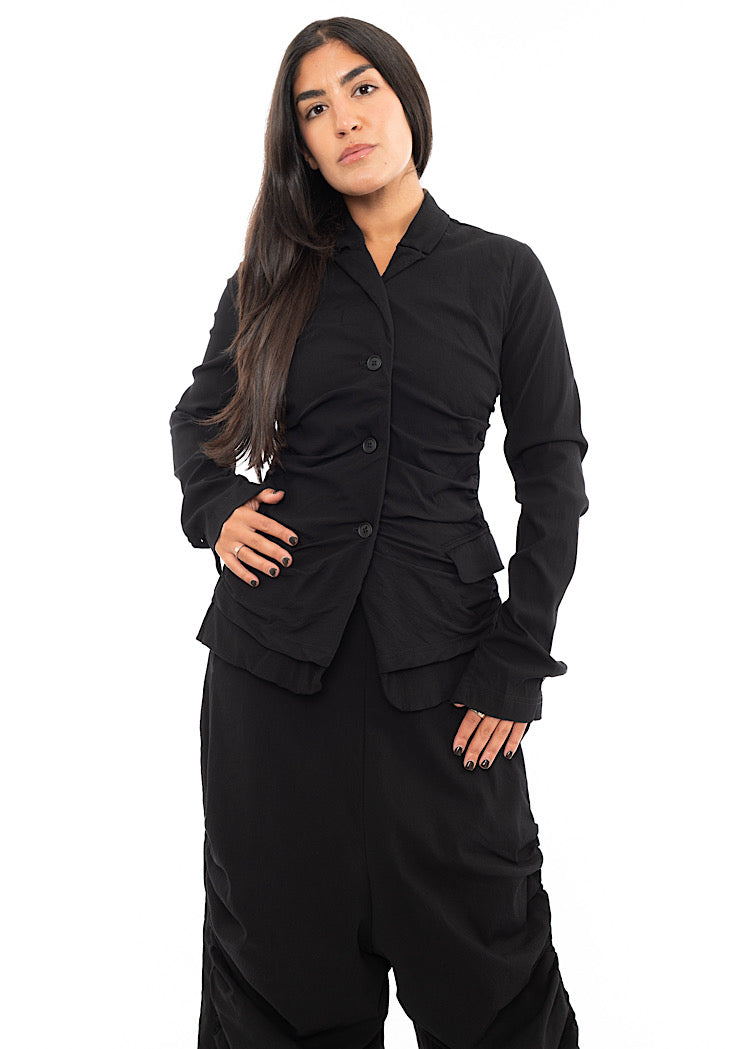 A Model wearing a minimalist techno Jacket with rouging details and distinct pockets. Paired with matching trousers, in a Black colour. 