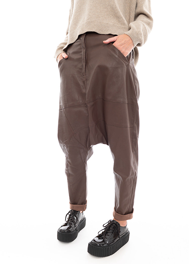 A Model wearing a Structured Drop-Crotch Brown Leather Trouser. Showing the fold up detail along the hem of the Trouser.