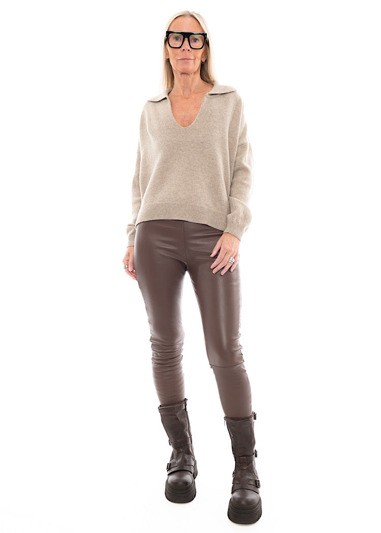 A Full size Photo of A Model wearing a tight fitting Brown Leather Trouser, paired with a grungy style boot and light coloured pullover.