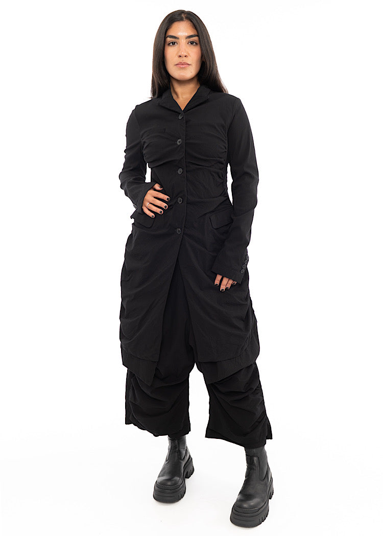 A full frame photo of A Model wearing a detailed techno coat and matching trousers, in a Black colour. Paired with a chunky soled Boot.