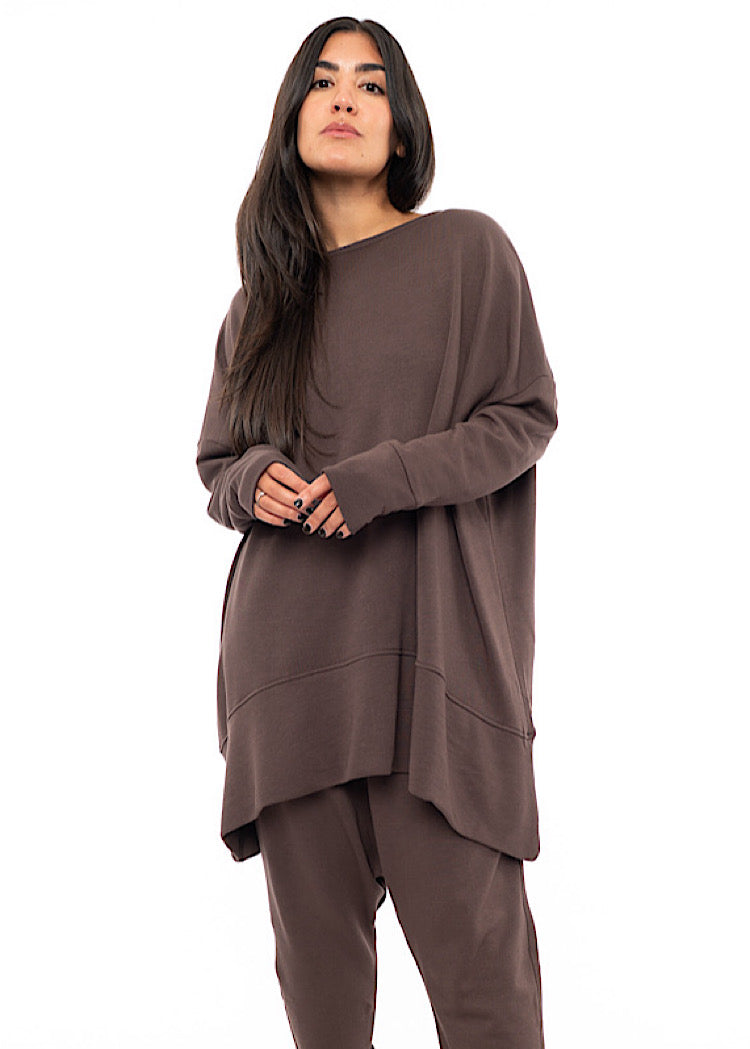 A Model wearing an oversized Plum toned Pullover, paired with a Matching Trouser. Showing the pieces long length of arm and body.